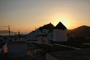 View of a beautiful white windmills,  while the sun is setting dramatically behind the village of Ios in Greece