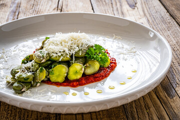 Broad beans salad in tomato sauce with parmesan on wooden table
