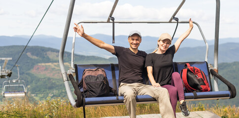 Man and a woman riding on the lift down the scenic Mountain during summer. Green tree forest surrounds the escalator. © Angelov