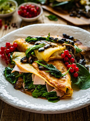 Crepes with spinach, fried mushrooms and pork ham on wooden table