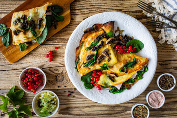 Crepes with spinach, fried mushrooms and pork ham on wooden table