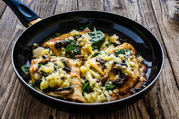 Crepes with spinach, fried mushrooms and pork ham in cooking pan on wooden table