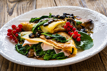 Crepes with spinach, fried mushrooms and pork ham on wooden table