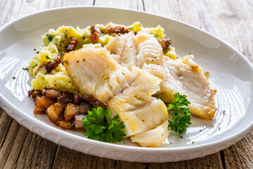 Fish dish - fried cod fillet with potato puree and bacon on wooden table
