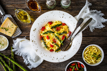 Pasta with asparagus, parmesan and tomatoes on wooden table
