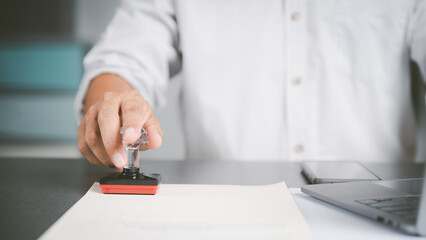 A young executive is stamping on documents for a business contract. Transaction and document management concepts include negotiating corporate entities and filling out legal forms or agreements.