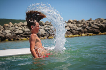 Fototapeta premium Handsome teenage boy swimming and having fun floating on a swim board in the sea on a hot summer day