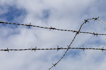Fototapeta na wymiar Steel fence and barbed wire detail with clouds and sky background