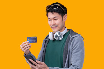 smiling cheerful asian male traveller in casual cloth hand gesture present show credit card  present blank space in hand isolated on yellow colour  background studio shot travel with cashless concept