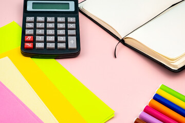 Various school materials, such as markers, coloured pens and markers, notebook and eraser. On top of a pink table. 