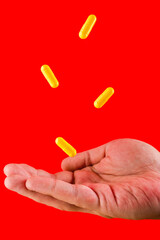 Male hand fully opened try to catch the yellow pills red background 