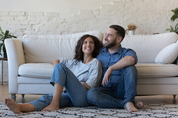 Happy dreamy married couple enjoying comfort, leisure at home, relaxing together on heating...
