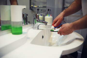 Hands with tooth brush and paste on blurred background in the bathroom in the sink. Selective focus.
