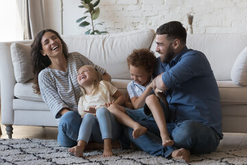 Happy parents cuddling, tickling little children on floor, laughing, having fun, enjoying family...