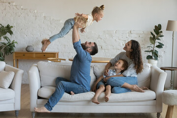 Happy young parents having fun with little kids, enjoying family leisure, activity on couch at...