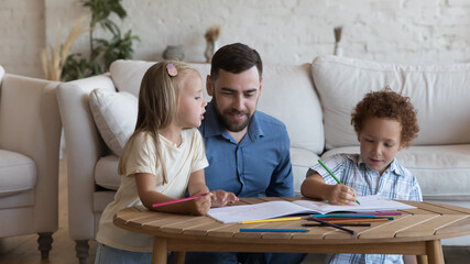 Happy dad enjoying creative leisure time with two sibling kids, watching children drawing in colorful pencils in album, talking, helping, giving support. Family playtime, fatherhood concept. Banner