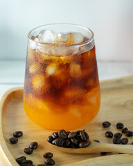 Close up of iced coffee with orange juice, placed on a wooden tray decorated with coffee beans, and white background.