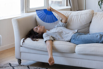 Exhausted young woman suffering from hot weather, overheat, too high air temperature at home, lying...