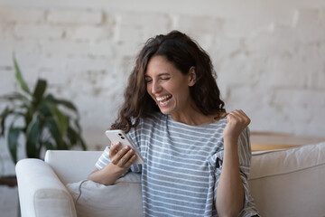 Excited smartphone user woman receiving good happy news, holding mobile phone, looking at screen,...