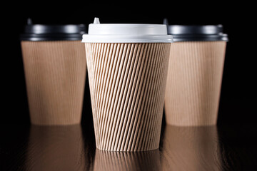Brown paper cup for hot coffee, tea, drinks with white and black lids on a black background.