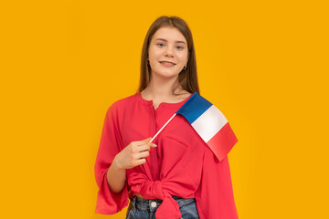 Portrait of cute young girl with the flag of France in her hands on orange background. Learn French. Immigration to France.
