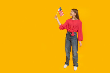 Young girl with an American flag in her hands. Full-length portrait of teenager on yellow background. Space for text