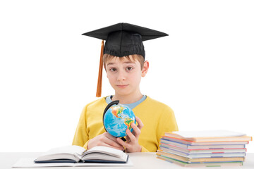 Surprised boy sitting at desk near copybooks with globe in hands. Doing homework. Foreign language...