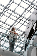 Girl stands on the balcony of modern building. Woman under the roof of futuristic building in high-tech style. Bottom view