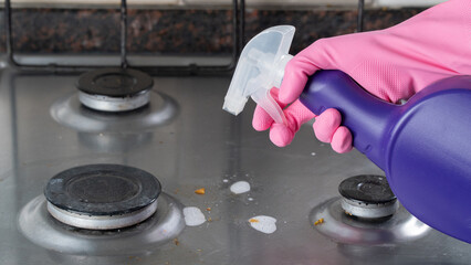 A woman's gloved hand sprays detergent on a dirty gas stove