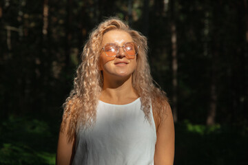 The young woman in sunglasses looking at the sun against the background of a dark forest