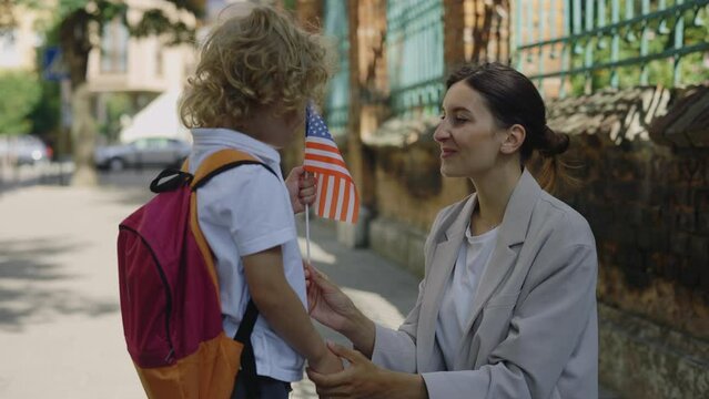 Mother talking to her son looking at child and giving american flag. Little smilling patriotic kid looking at female adult and taking the usa flag. Patriotic and education concep
