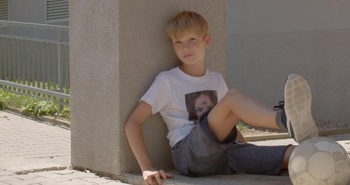 Portrait of preteen boy with ball sitting alone, summer outdoor. Communication and interaction problems in children with autism spectrum.