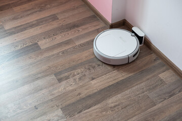 Robotic vacuum cleaner on laminate wood floor charging from base station. Smart cleaning...