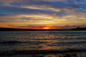 Obraz premium sunset over the lake, bright sun reflected in the waves, glare on the water, beautiful summer landscape