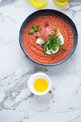 Bowl of salmorejo or cold spanish tomato soup with jamon, top view on a light-grey marble background, vertical shot