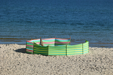 Parasol słoneczny na plaży nadmorskiej w wakacje razem z parawanem na wiatr.
