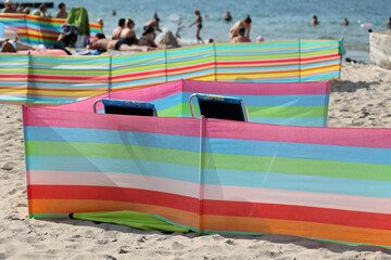 Parasol słoneczny na plaży nadmorskiej w wakacje razem z parawanem na wiatr.
 - obrazy, fototapety, plakaty