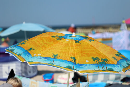 Parasol słoneczny na plaży nadmorskiej w wakacje razem z parawanem na wiatr.
