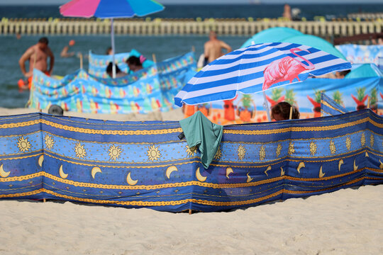 Parasol słoneczny na plaży nadmorskiej w wakacje razem z parawanem na wiatr.
