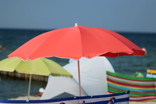 Parasol słoneczny na plaży nadmorskiej w wakacje razem z parawanem na wiatr.
