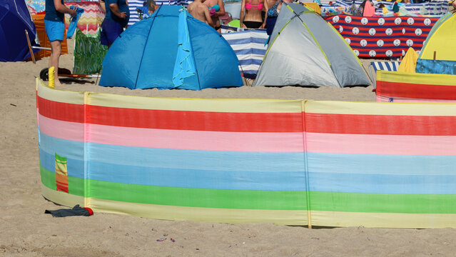Parasol słoneczny na plaży nadmorskiej w wakacje razem z parawanem na wiatr.
