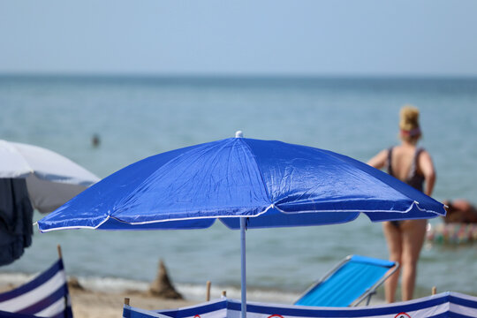 Parasol słoneczny na plaży nadmorskiej w wakacje razem z parawanem na wiatr.
