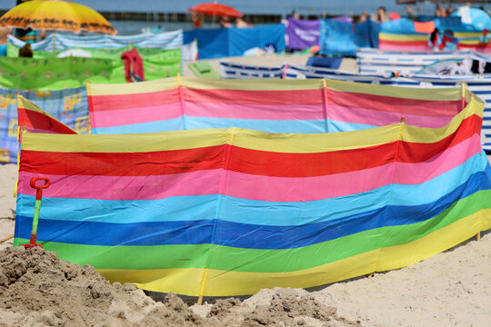 Parasol słoneczny na plaży nadmorskiej w wakacje razem z parawanem na wiatr.
