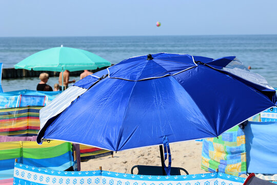 Parasol słoneczny na plaży nadmorskiej w wakacje razem z parawanem na wiatr.

