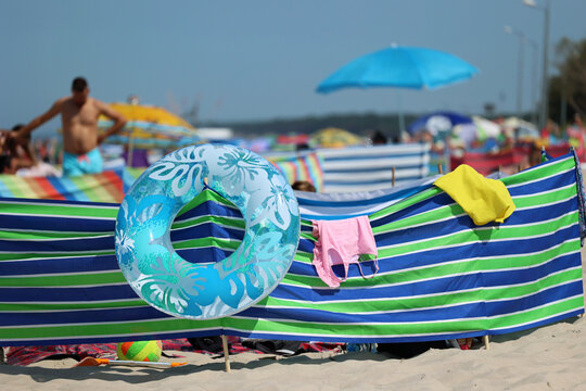 Parasol słoneczny na plaży nadmorskiej w wakacje razem z parawanem na wiatr.
