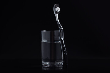 A black and white toothbrush and glass of mouthwash on black background with copy space.