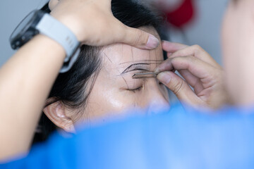 The process of shaping eyebrows by a beauty master with a thread for a young asian lady - Eyebrows microblading concept. Micropigmentation eyebrows work flow in a beauty salon. 