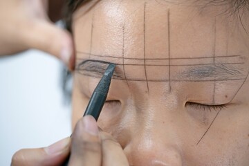 The process of shaping eyebrows by a beauty master with a thread for a young asian lady - Eyebrows microblading concept. Micropigmentation eyebrows work flow in a beauty salon. 