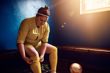 Young goalie adjusting her soccer socks in dressing room.