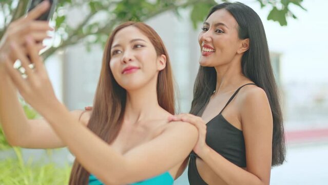 Beautiful healthy asian women wear dress are making selfie with smartphone.They are standing near a swimming pool and smiling.